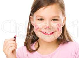 Little girl is applying lipstick on her cheek