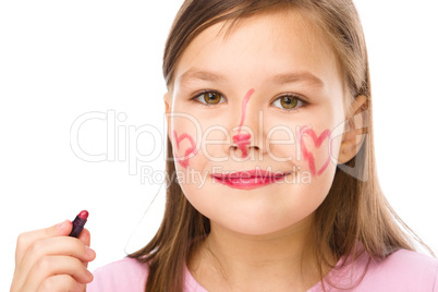 Little girl is applying lipstick on her cheek