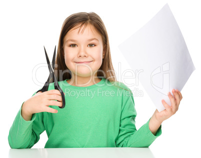 Little girl is cutting paper using scissors