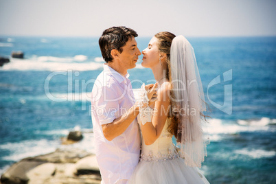 Elegant smiling bride and groom walking on the beach, kissing, wedding ceremony, Mediterranean Sea.