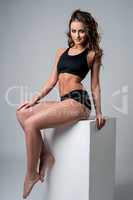 Beautiful tanned brunette posing sitting on cube