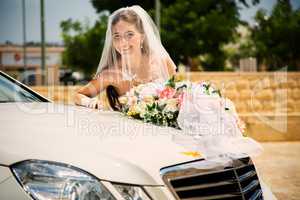 Happy bride with bouquet near wedding car