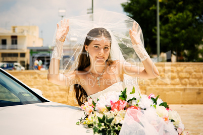 Happy bride with bouquet near wedding car