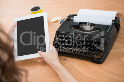 Hipster woman using a tablet beside her typewriter