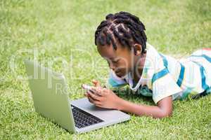 A kid looking his mobile phone and laptop
