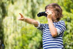 Portrait of cute boy looking with binoculars and pointing someth