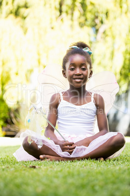 Cute mixed-race girl sitting and wearing a fairy dress on a park