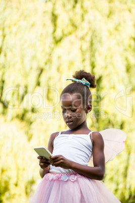 Cute mixed-race girl wearing a fairy dress and using a smartphon