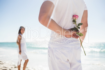 Close up of man holding a rose behind him