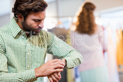 Bored man waiting his wife while woman by clothes rack