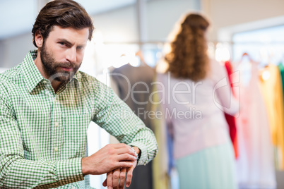 Bored man waiting his wife while woman by clothes rack