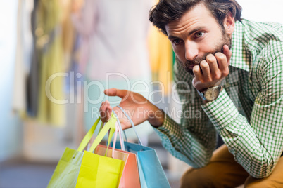 Bored man with shopping bags while woman by clothes rack