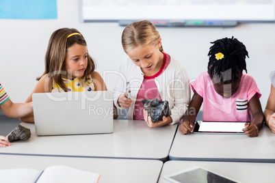 Pupil looking at rock with magnifying glass and classmates using