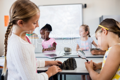 Profile view of girls looking at rock with magnifying glass