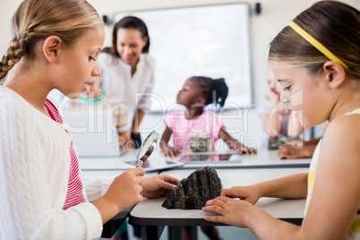 Side view of girls looking at rock with magnifying glass