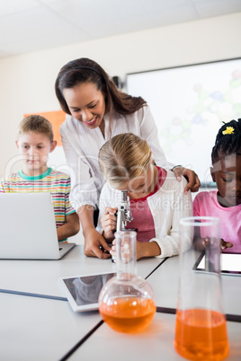 Cute pupil looking through microscope with teacher