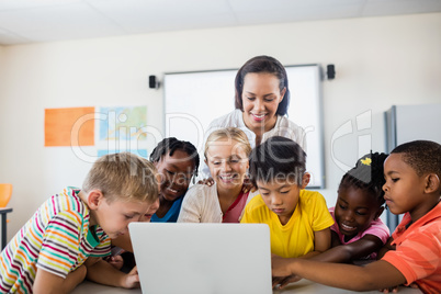 Happy teacher and pupils using laptop