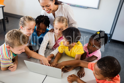 Happy teacher and pupils using laptop