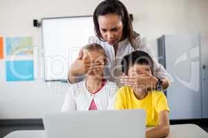 Teacher covering pupils eyes in front of computer