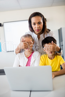 Teacher covering pupils eyes in front of computer and looking at