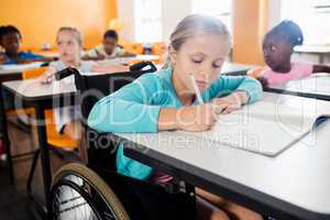 Portrait of a cute pupil in wheel chair working at desk