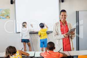 Smiling teacher using a tablet while pupils are working