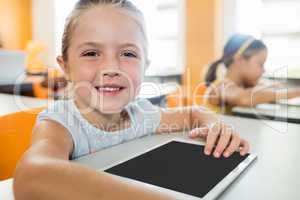 Cute girl posing at desk with tablet pc in classroom