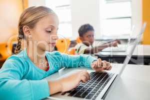 Side view of little girl using laptop in classroom