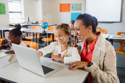 Teacher helping pupil with laptop