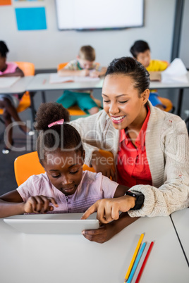 School girl using tablet at desk with her teacher
