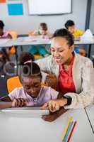 School girl using tablet at desk with her teacher