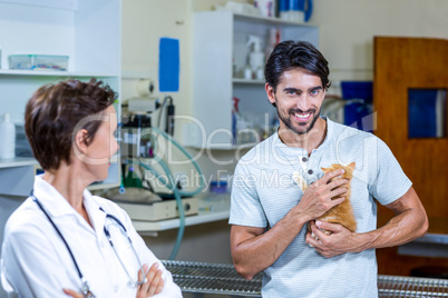 Man smiling and holding a kitten with woman vet