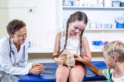 Little girl holding a rabbit surrounded bay little boy and woman
