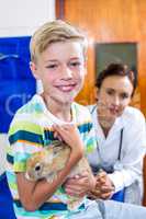 Portrait of little boy holding a rabbit in front of woman vet