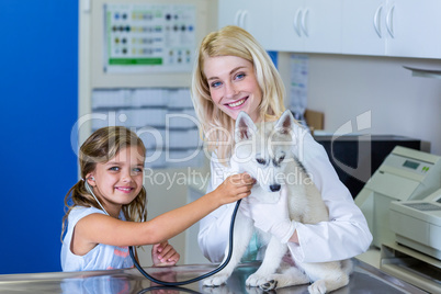 Little girl examining a puppy with a stethoscope with the woman