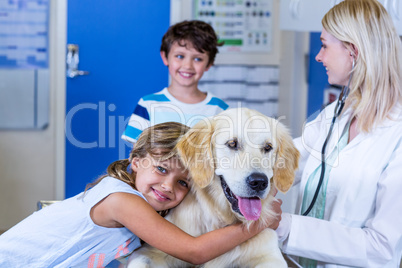 Little girl giving a hug to her dog in front of a boy and woman