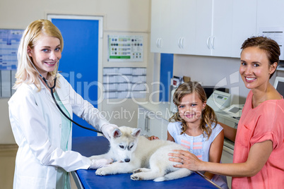 Woman vet smiling and examining a cute puppy with owners