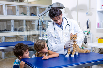 Vet taking care of a cat while two children are looking at the c