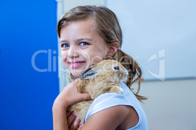 A cute little girl looking at the camera is hugging her rabbit i