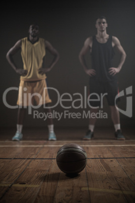 Basketball players posing with hands on hips behind a ball