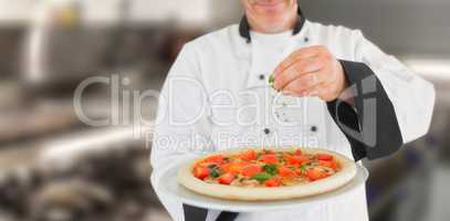 Composite image of portrait of a chef holding a pizza and adding herbs