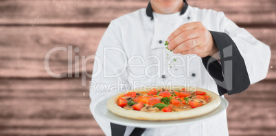 Composite image of portrait of a chef holding a pizza and adding herbs