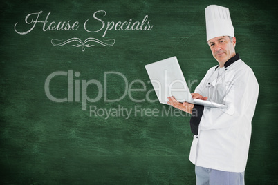 Composite image of chef standing holding a laptop