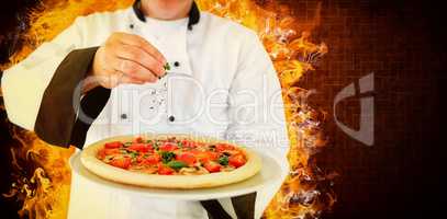 Composite image of portrait of a chef holding a pizza and adding herbs
