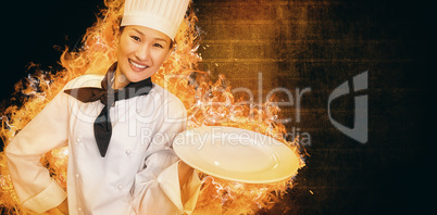 Composite image of smiling female cook holding empty plate in kitchen