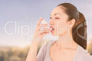 Composite image of asthmatic pretty brunette using inhaler