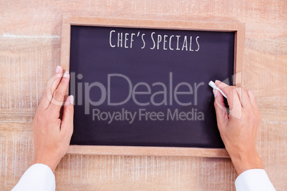Composite image of chef hand writing on a chalkboard