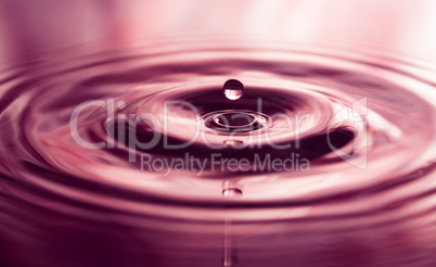 Macro photo of water drops falling into a pool of water, causing a splash and ripples.