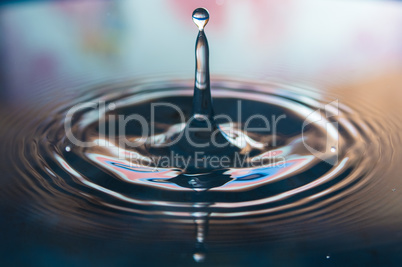 Macro photo of water drops falling into a pool of water, causing a splash and ripples.