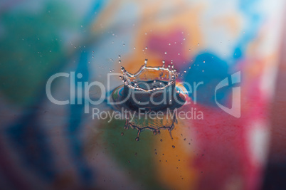 Macro photo of water drops falling into a pool of water, causing a splash and ripples.